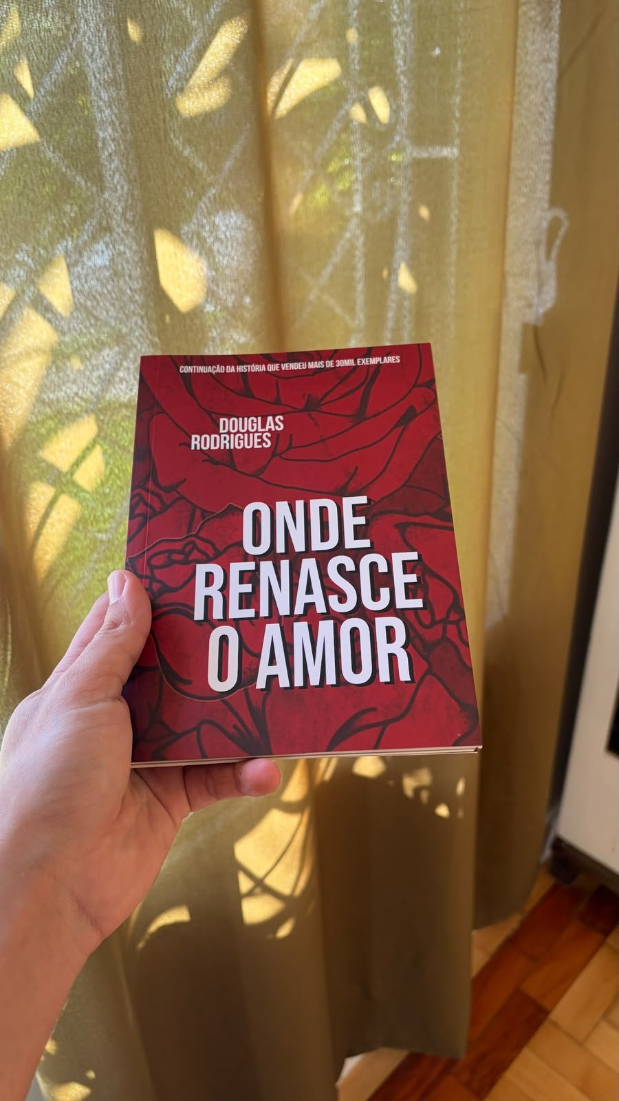 Onde Renasce o Amor, de Douglas Rodrigues, segurado diante de uma cortina iluminada.